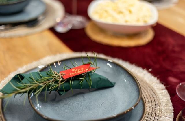 Prato azul com guardanapo verde e ramo de alecrim em mesa de Natal