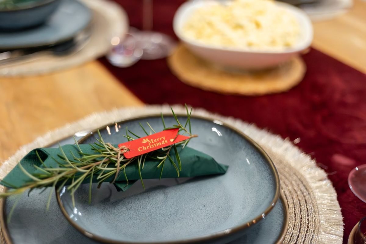 Prato azul com guardanapo verde e ramo de alecrim em mesa de Natal
