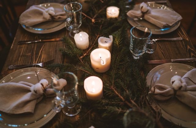 Mesa de Natal com pratos, guardanapos amarrados, velas e ramos de pinheiro