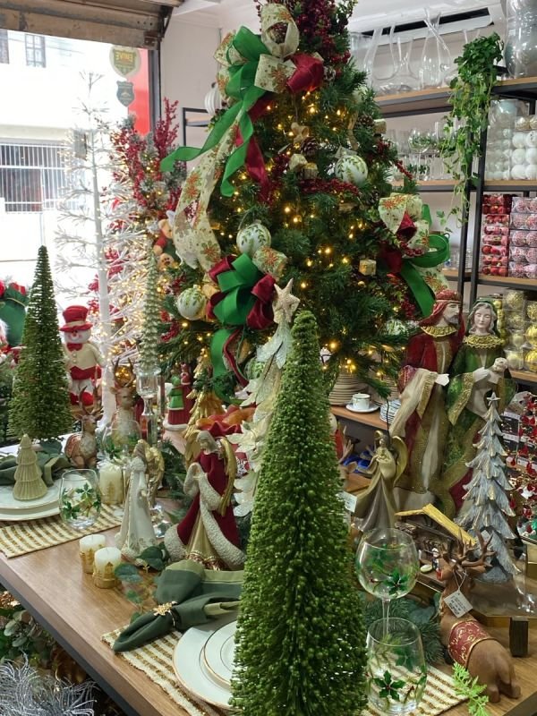Árvore de Natal com laços e luzes sobre mesa posta decorada, exemplo de decoração para loja